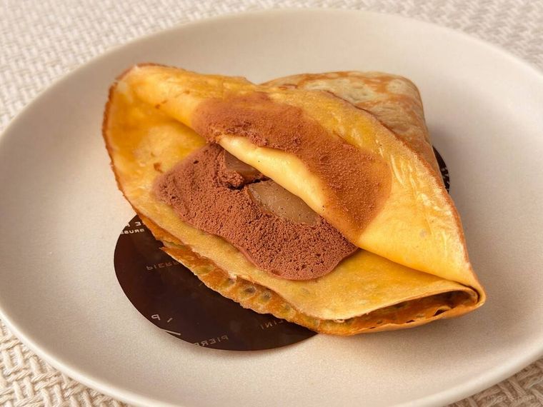 白皿に盛り付けられたショコラと洋梨のクレープがテーブルの上に置かれている様子