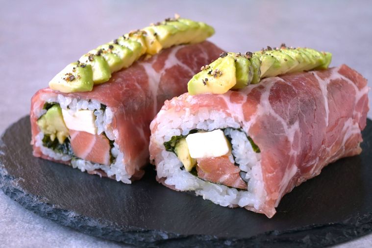 黒いスレート皿に盛り付けられた2本の生ハムロール寿司