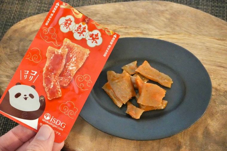 木のカッティングボードと黒い皿にのった麻辣味の蒟蒻おつまみと赤いパッケージ