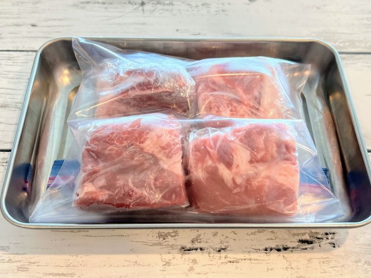フリーザーバッグに入れてアルミトレイの上に置き、冷凍保存の準備をされた豚かたまり肉