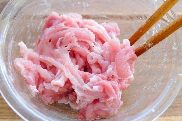 ガラスのボウルに入った豚こま肉に片栗粉をまぶす様子