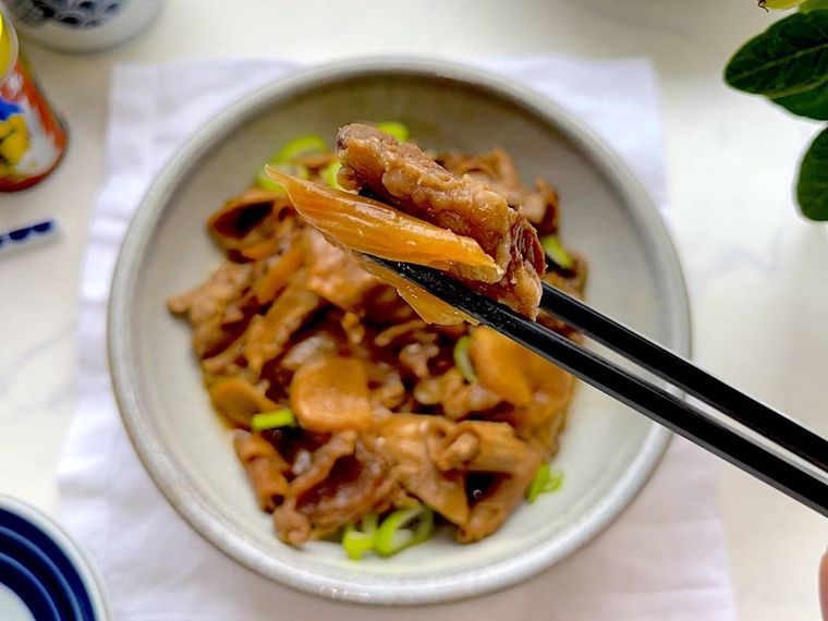 牛すじの煮込みとネギをひと口分箸で持ち上げているところ