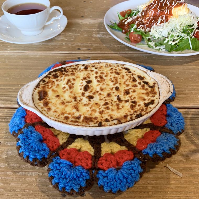 ニットのランチョンマットに置かれたグラタンと白い器に盛られたタコライスと紅茶