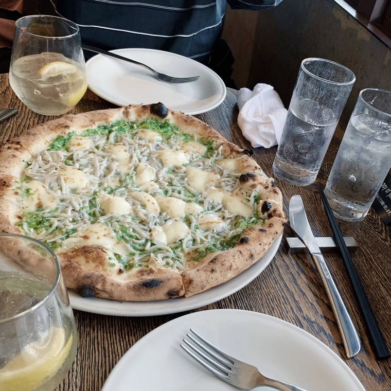 テーブルにのったピザ1枚と取り皿とグラス