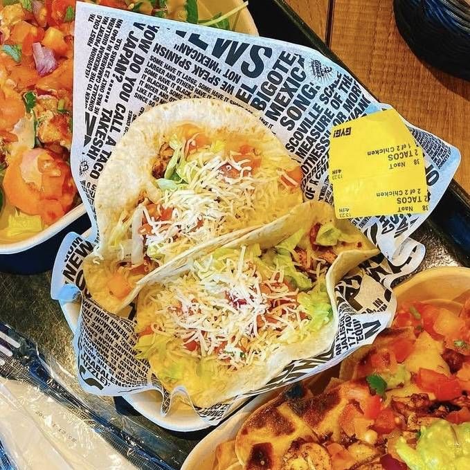 おしゃれな紙に包まれた、野菜やお肉たっぷりのタコス2個