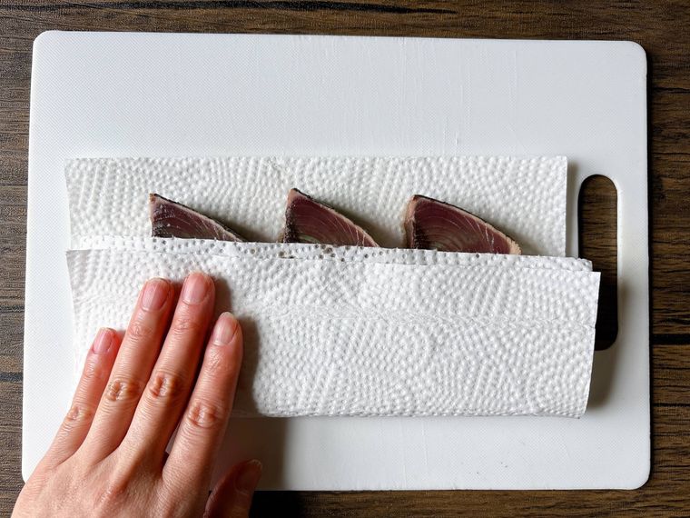 キッチンペーパーでカツオのたたきの水気を拭く様子