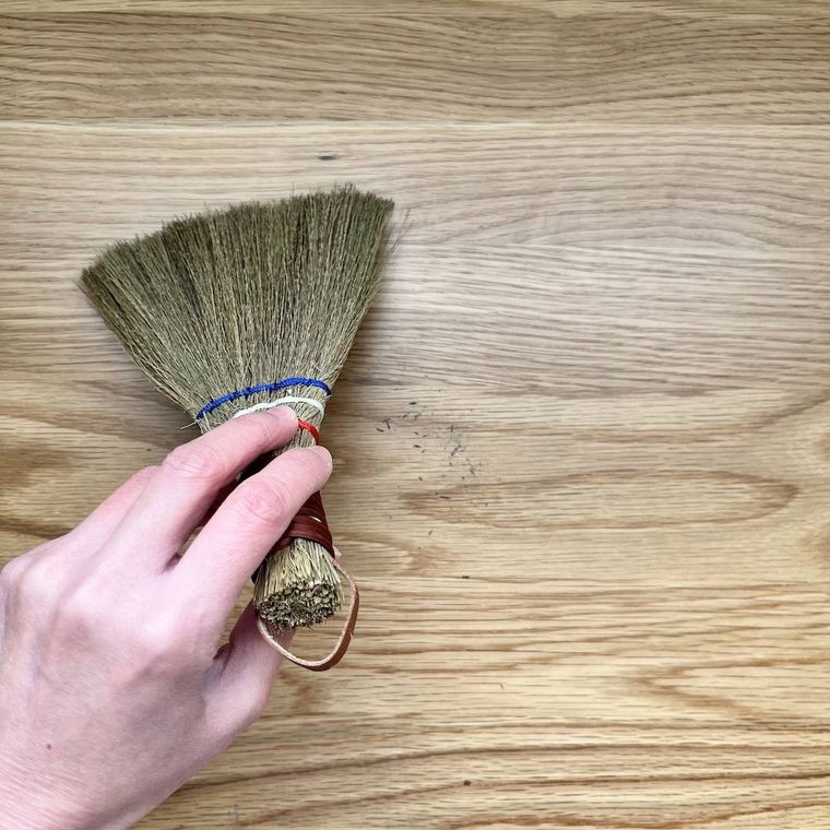 セリアのシダ製ミニほうきでデスクを掃除している