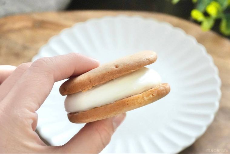 木のカッティングボードにのった白い皿とビスケットサンドを持つ手