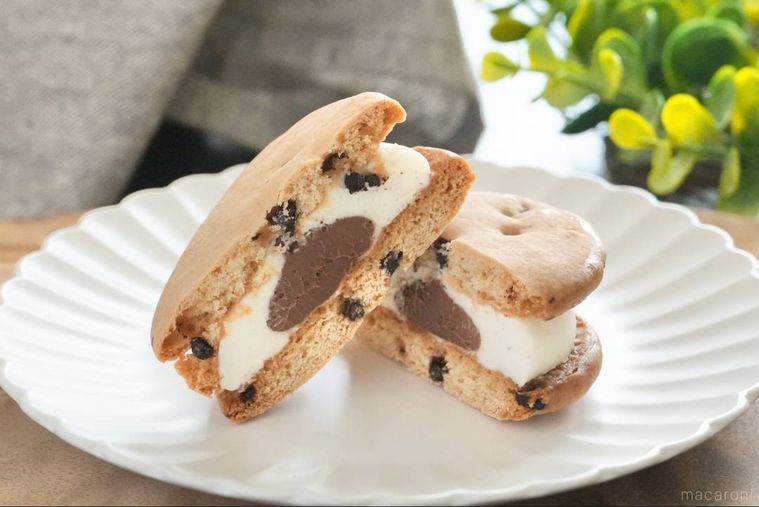 木のカッティングボードと白い皿にのったチョコチップビスケットとガナッシュとクリームのスイーツサンドの断面