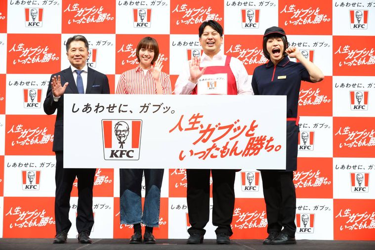 KFCのイラストの前でポーズをとる4人