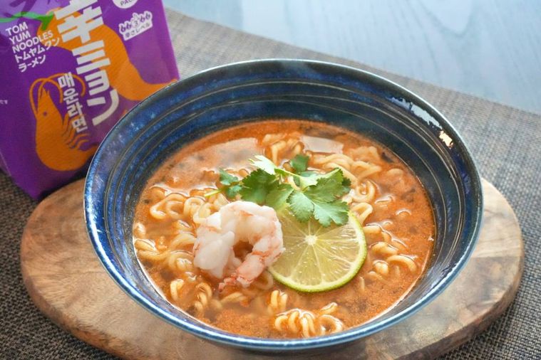 木のカッティングボードにのった青い丼に盛られたトムヤムクンインスタントラーメン