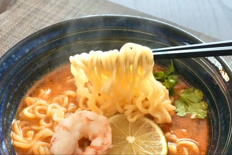 トムヤムクンインスタントラーメンの麺を黒い箸で持ち上げる様子