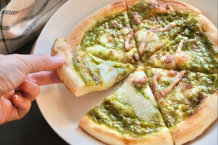 白い器にのったジェノベーゼ冷凍ピザをカットして手で持ち上げる様子