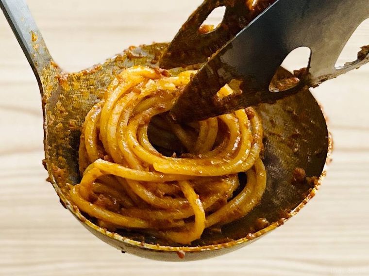 トングとお玉でボロネーゼパスタを巻いている様子