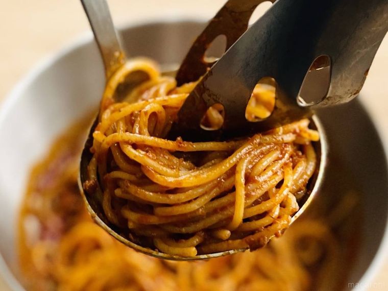 トングとお玉でボロネーゼパスタを巻いている様子