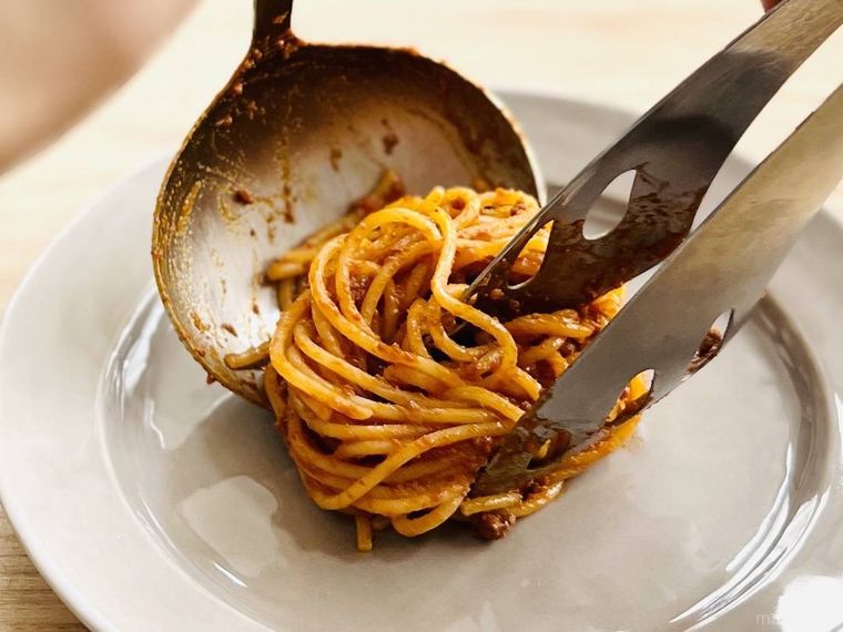 ボロネーゼパスタを皿に盛り付けている様子