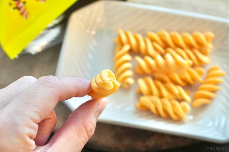 ツイスト形状のコーンスナックを手に持ってかじる様子