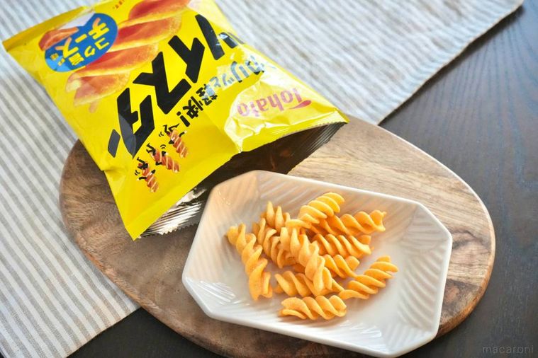 木のカッティングボードと白い皿にのったチーズ味のコーンスナックと黄色のパッケージ