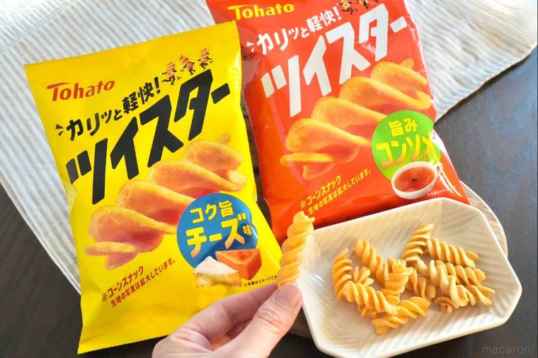 黄色とオレンジ色のパッケージのコーンスナックと白い小皿とスナックを持つ手