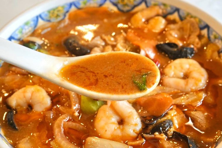 麻辣麺のスープを白いれんげですくう様子