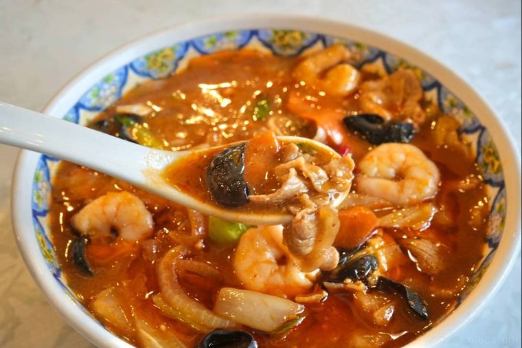 中華料理店の麻辣麺の具材を白いれんげですくう様子