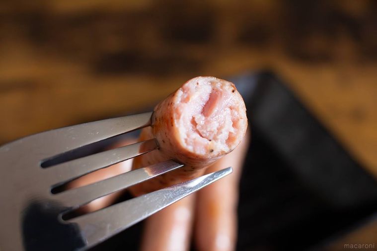 半分に割った丸大食品燻製屋 熟成あらびきウインナー 燻製ブラックペッパーをフォークで箸上げしている様子