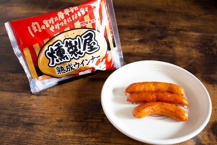 丸大食品燻製屋 熟成あらびきウインナー 旨辛チョリソーのパッケージと調理したウインナーを盛り付けたお皿が並んでいる