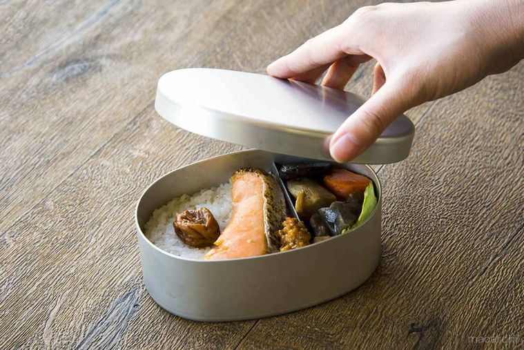 野菜の煮物や焼き鮭が入った仕切り付きのお弁当箱のふたを開けている様子