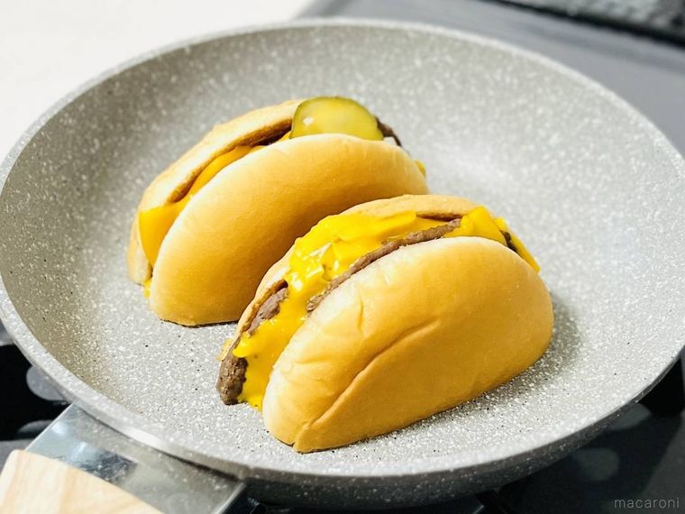 半分にカットしたダブルチーズバーガーをフライパンで焼いている様子