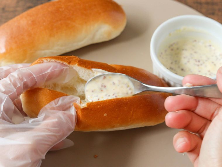 ロールパンにマスタードマヨネーズを塗っている
