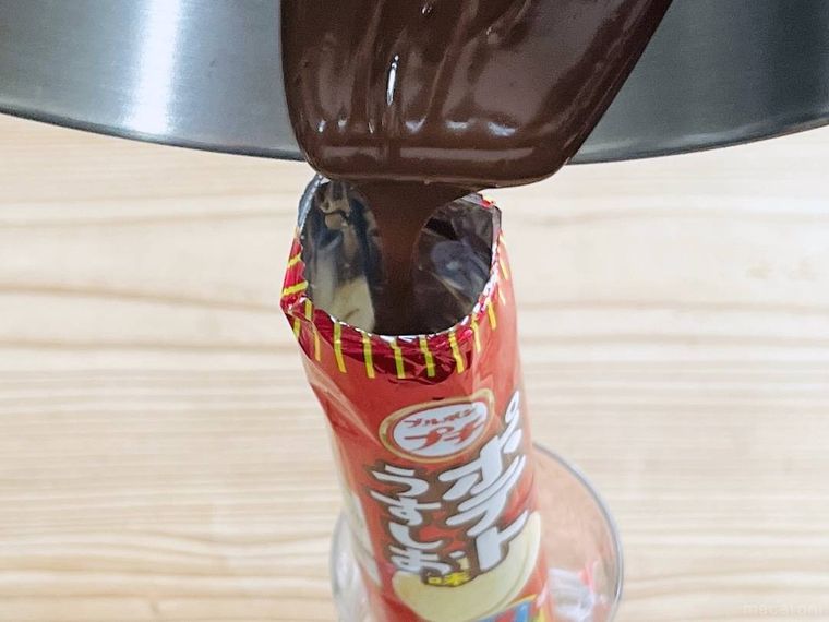 プチポテトうすしお味の袋に溶かしたチョコレートをそそいでいる様子