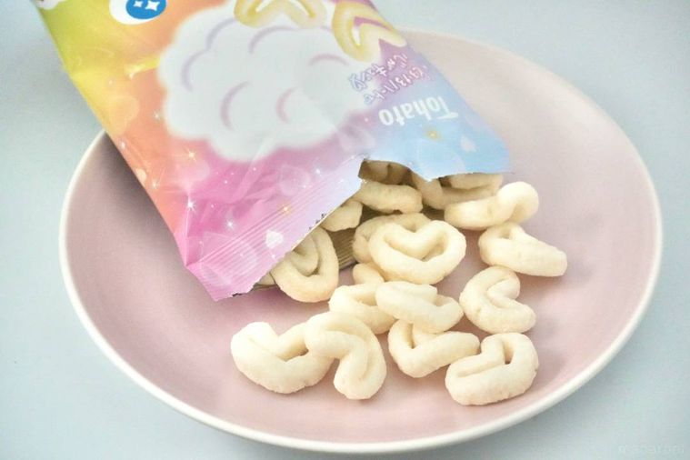 虹色のパッケージから白いハート型のキャラメルコーンをピンク色の皿に出す様子