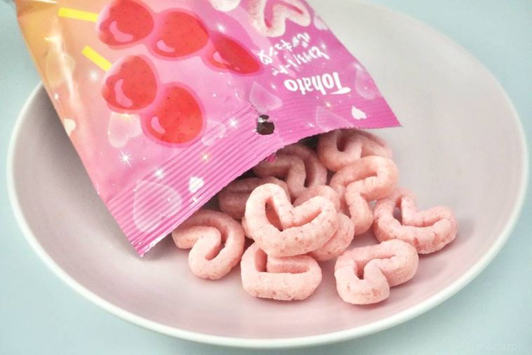 ピンク色のパッケージからピンク色のハート型のキャラメルコーンをピンク色の皿に出す様子