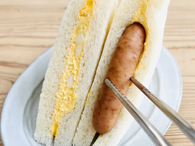 コンビニのたまごサンドに、丸大食品の燻製屋熟成あらびきポークウインナーを挟んでいる様子