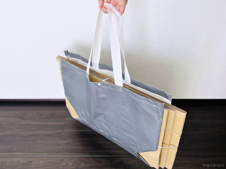 グレーのppバッグでダンボールを挟み、持ち上げている様子