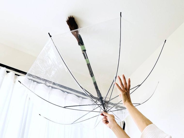 ほうきを貼りつけた傘で天井を掃除している様子