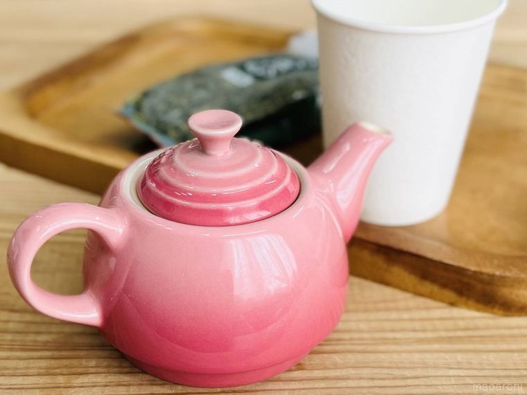 テーブルにピンク色の急須、紙コップ、茶葉が置かれている様子
