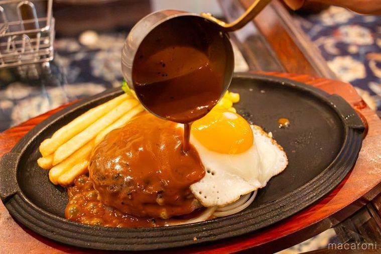 ロイヤルホスト黒黒ハンバーグブラウンバターソース目玉焼き付250gのブラウンバターソースをかけている様子