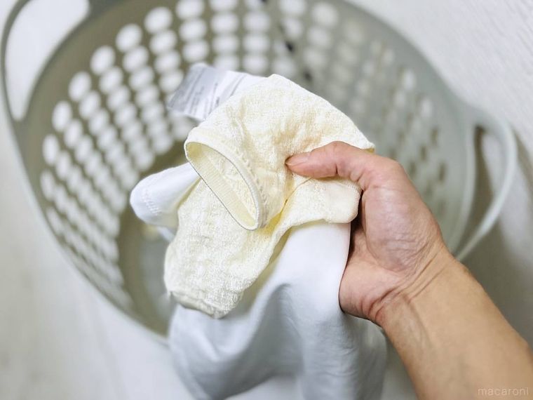 裏返した白い靴下と肌着を洗濯かごに入れようとしている様子