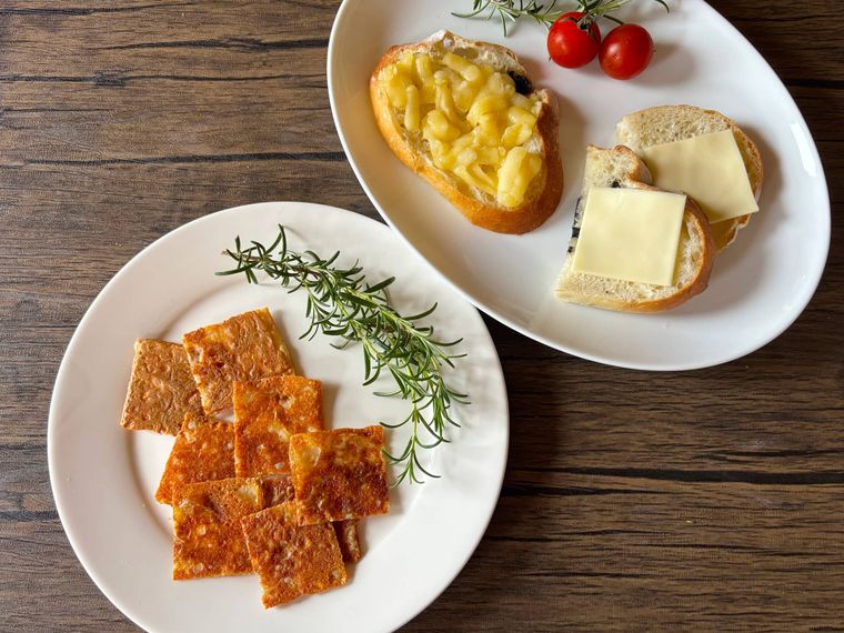 白色の皿に盛られたとろけるチーズを焼いたもの、パンにのせたもの