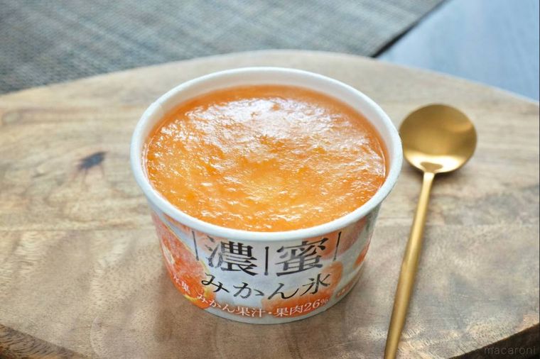 木のカッティングボードにのったみかん果肉入りのかき氷カップと金のスプーン