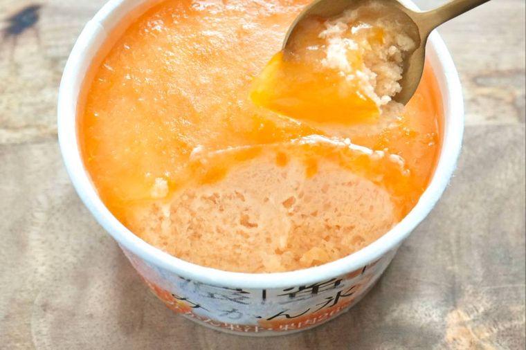 木のカッティングボードにのったみかん果肉入りのかき氷を金のスプーンですくう様子