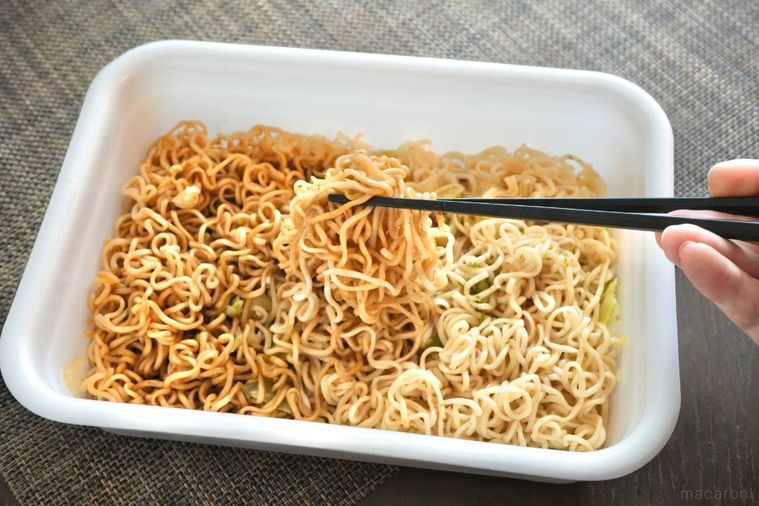 白い容器に盛られたソース味と塩味の焼きそばを黒い箸で混ぜ合わせる様子