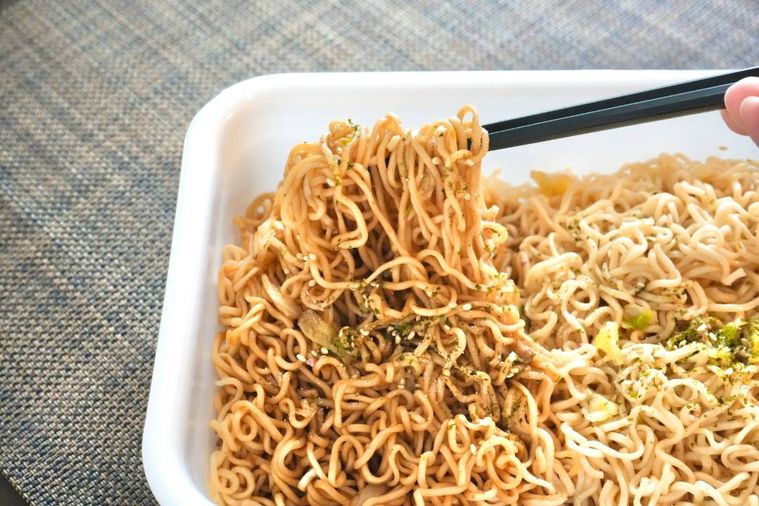 白い容器からソース焼きそばを黒い箸で持ち上げる様子