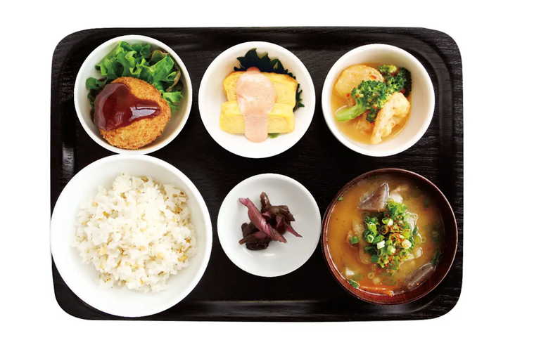 黒いトレーに小鉢やおかずと白米、味噌汁が並べられた様子