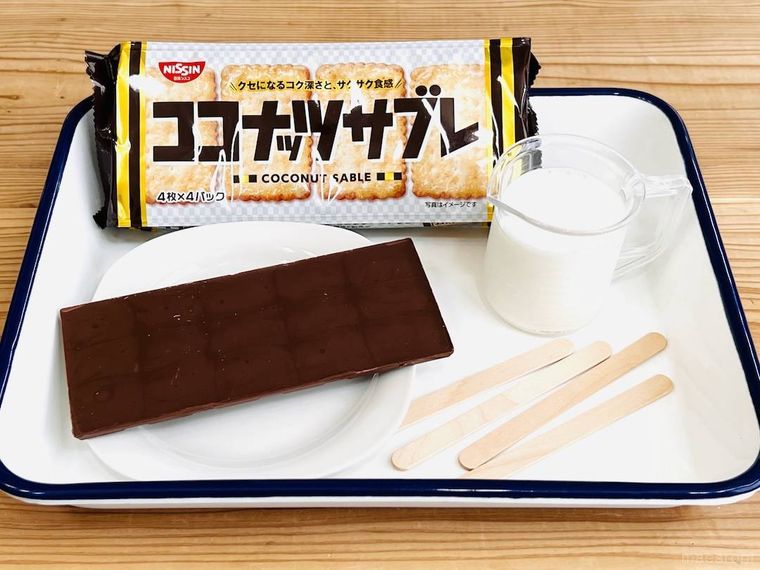日清シスコのココナッツサブレ、板チョコレート、牛乳、アイスの棒がバットに並んでいる様子