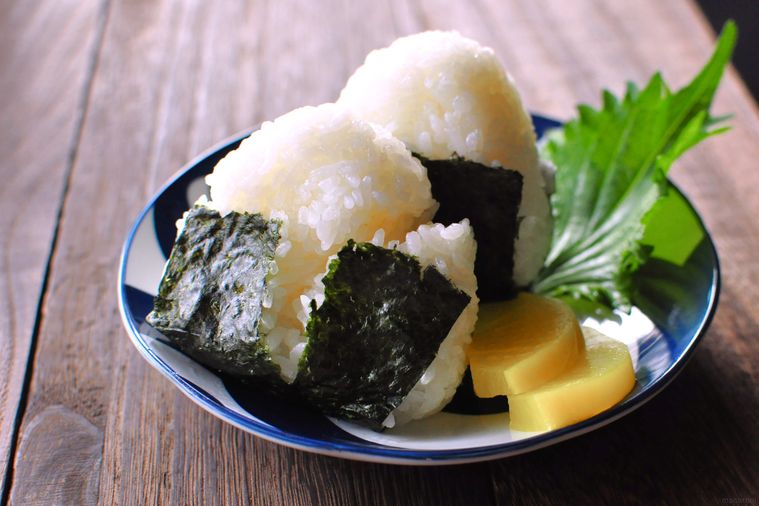 おにぎりが2つ皿に盛り付けられていて横にたくあんと大葉が添えてある