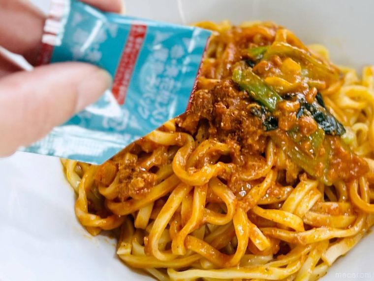 ファミリーマートのもちっと麺と濃厚だれの汁なし担々麺に唐辛子を振りかけている様子