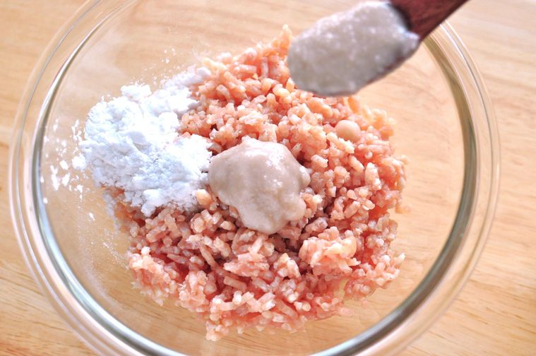 ひき肉と片栗粉が入ったガラスボウルに生姜麹をスプーンで入れる様子