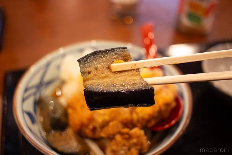 丸亀製麺鬼おろし鶏からぶっかけうどんにトッピングされたなすの揚げびたしを箸上げしている様子